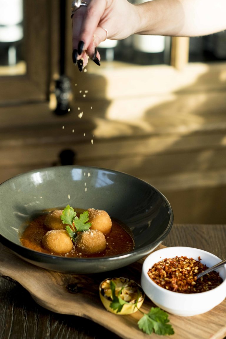 a hand sprinkling cheese onto arancini