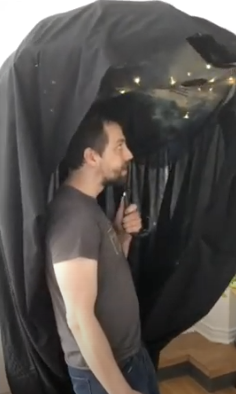 a man standing under an umbrella, indoors, a blanket is around the umbrella